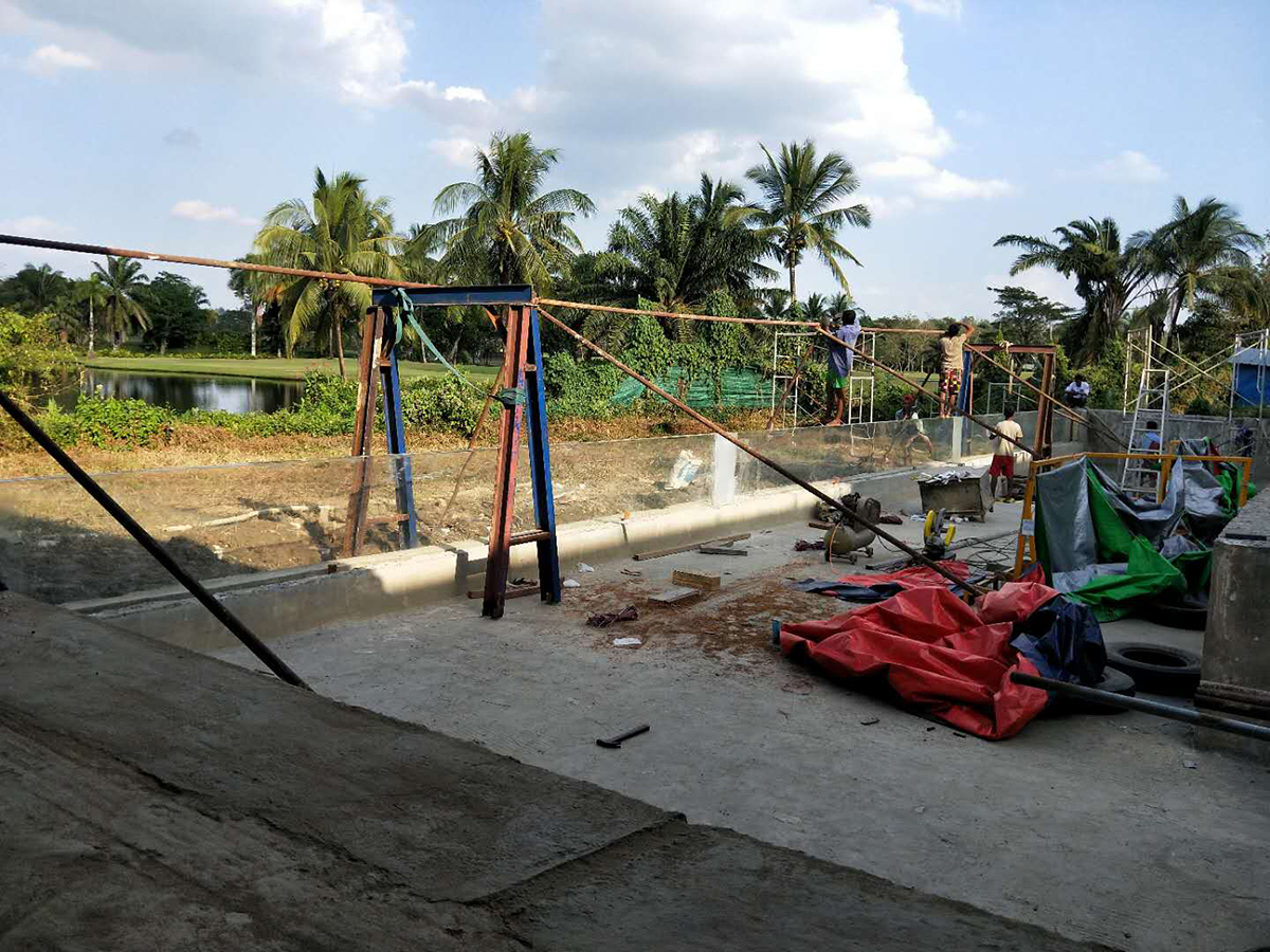 Installation-stage view of the Myanmar acrylic pool wall with temporary lifting support and workers on site
