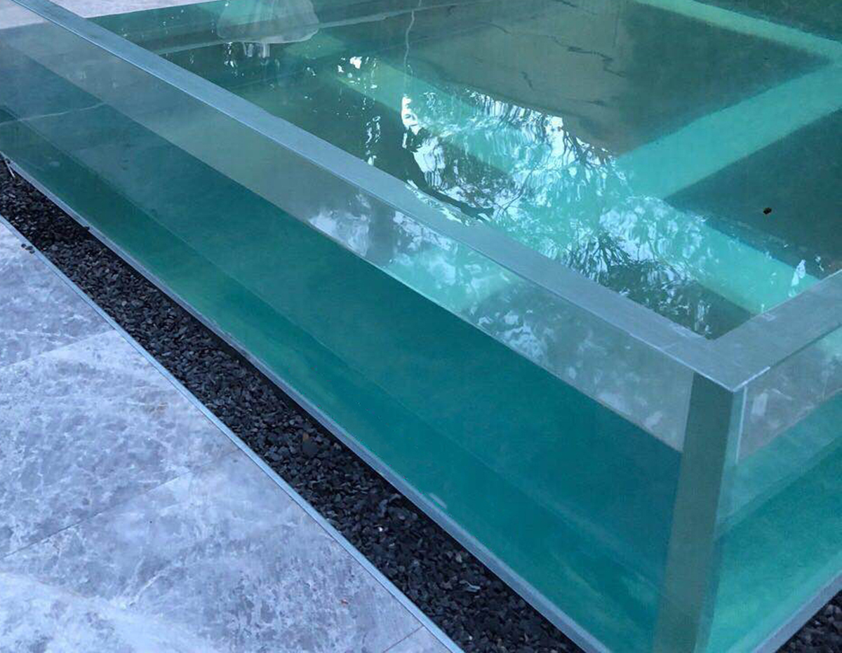 Freestanding transparent acrylic pool — four-sided panel construction showing corner joints, panel thickness, and base support condition